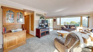 A spacious living room with a large wooden cabinet, a television, and a cozy seating area with a view of the outdoors. - Hot Tub, Views & Private Dock: Polson Haven! (Polson)