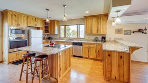 A spacious kitchen with wooden cabinets, stainless steel appliances, and a large island with stools. - Hot Tub, Views & Private Dock: Polson Haven! (Polson)