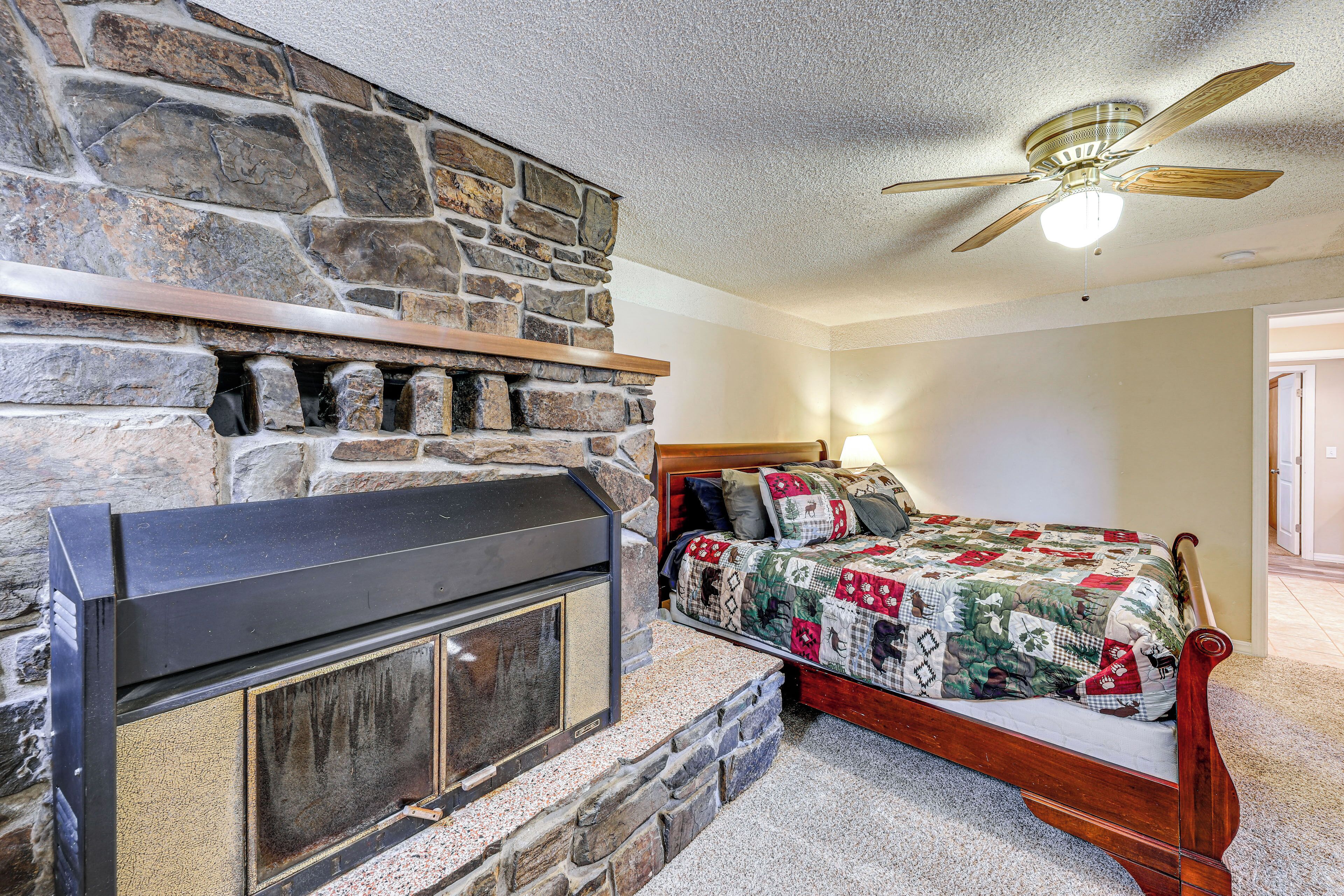 A bedroom with a stone fireplace, a bed with a quilt, and a ceiling fan.