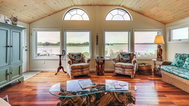 A spacious living room with a wooden ceiling, large windows overlooking a body of water, two armchairs, a glass coffee table, and a wicker sofa. - Dock + Water Access: Charlestown Beach Escape! (Charlestown)