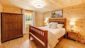 A wooden-paneled bedroom with a bed, nightstands, a wardrobe, and a window with curtains. - Secluded Mtn-view Cabin 16 Mi to Swan Lake! (Bigfork)
