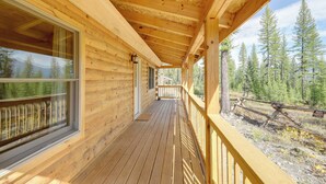A wooden cabin with a covered porch, large windows, and a view of a forest. - Secluded Mtn-view Cabin 16 Mi to Swan Lake! (Bigfork)