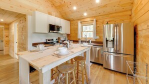 A wooden cabin with a kitchen featuring a stainless steel refrigerator, wooden cabinets, and a central island with stools. - Secluded Mtn-view Cabin 16 Mi to Swan Lake! (Bigfork)