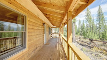 A wooden cabin with a covered porch, large windows, and a view of a forest.