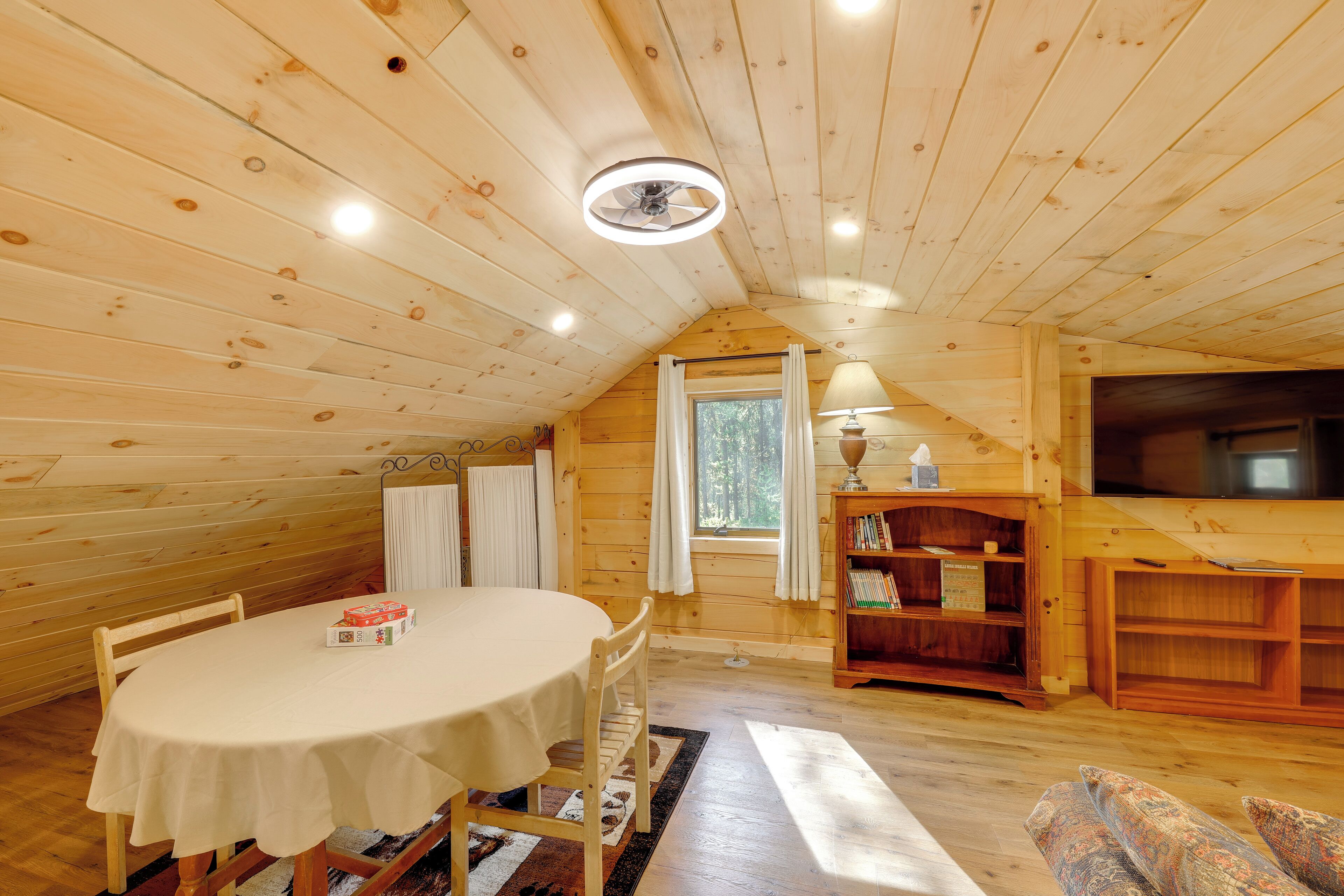 A cozy wooden interior with a round table, chairs, a bookshelf, and a television.