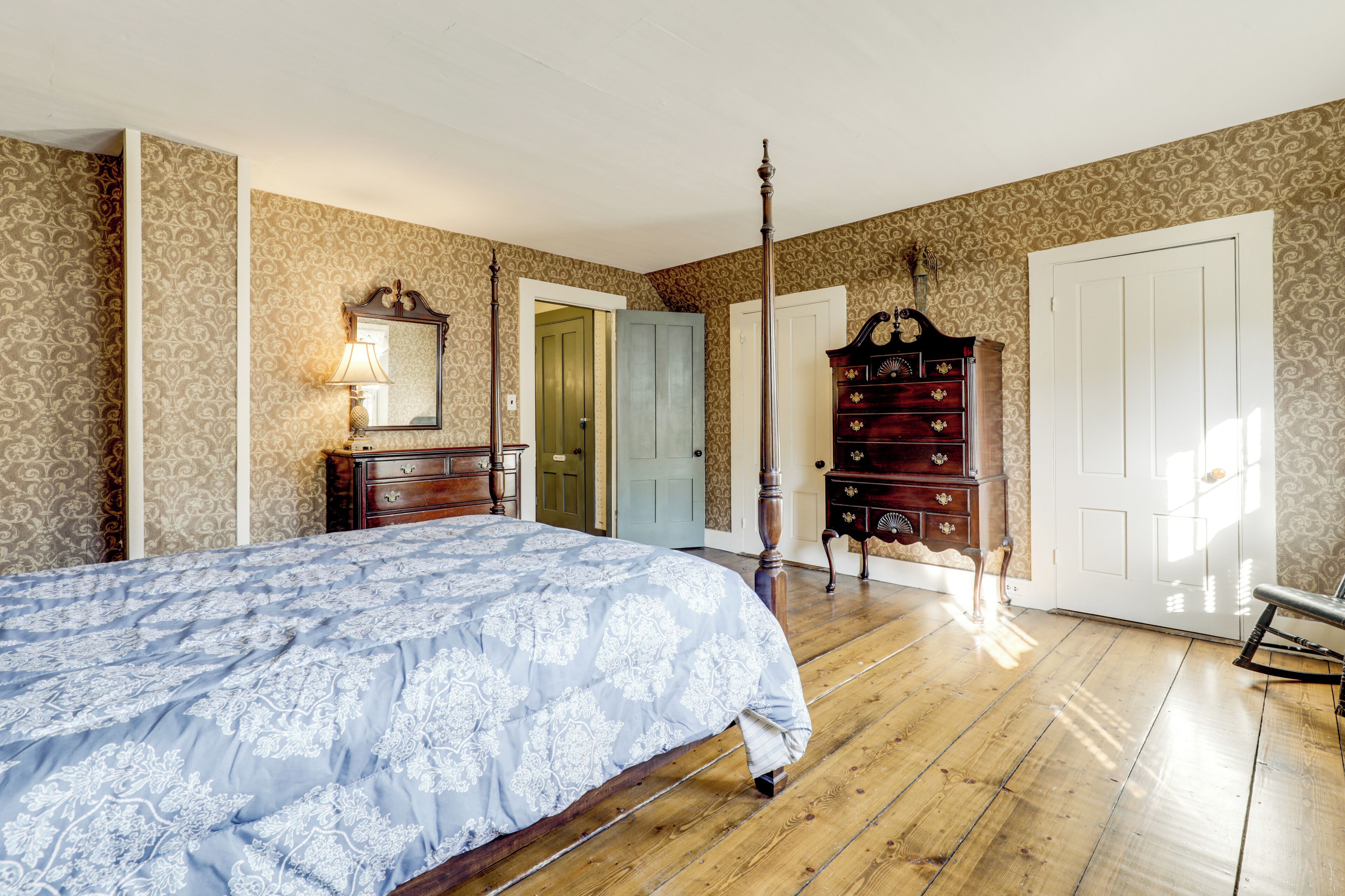 A bedroom with a four-poster bed, a wooden dresser, and a door leading to another room.