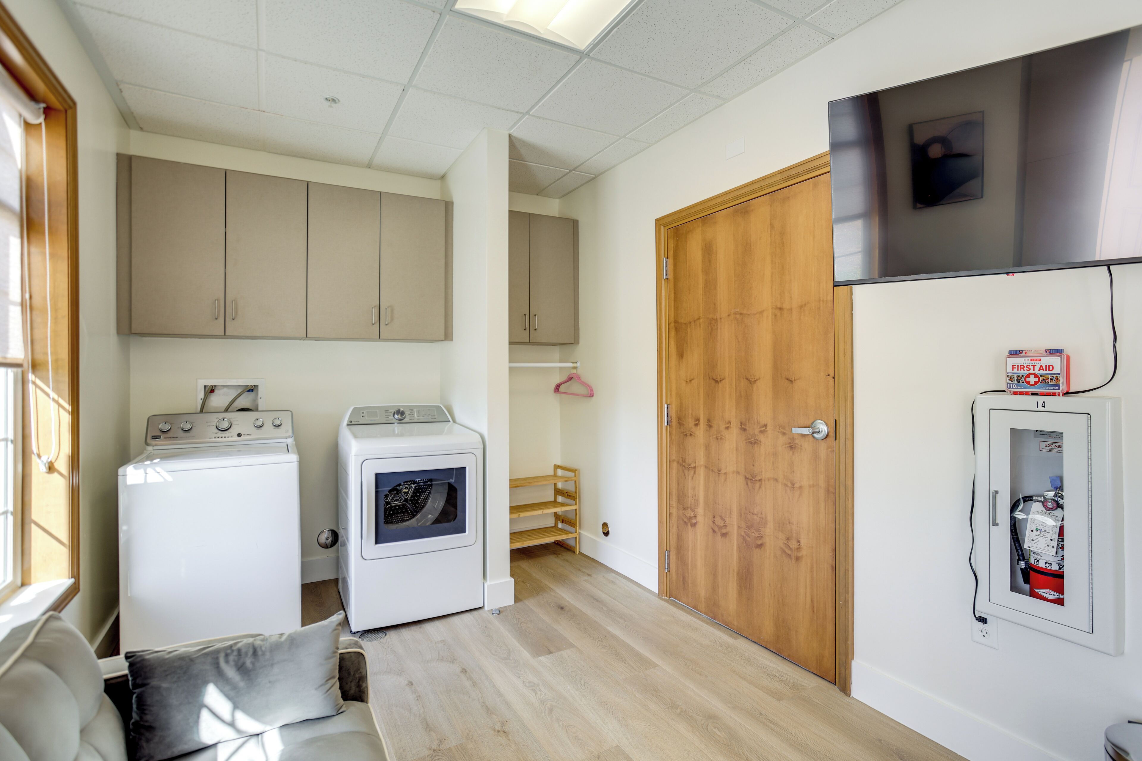 A compact laundry room with two washing machines, a wooden door, and a first aid kit on the wall.