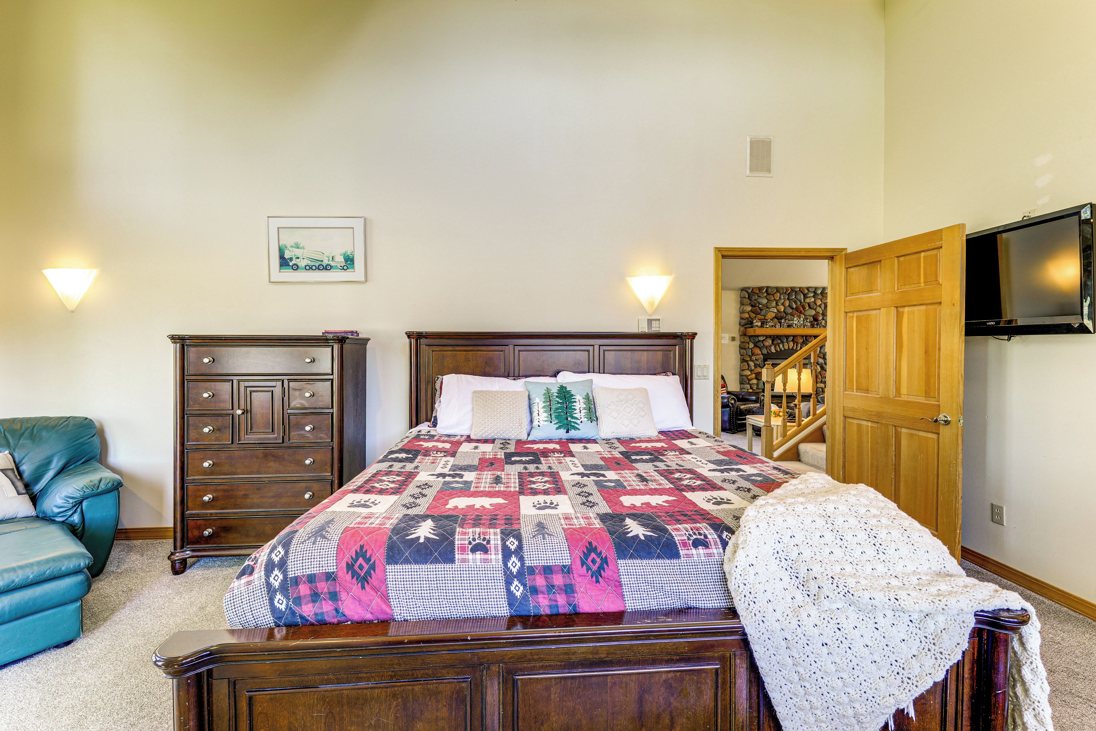 Une chambre à coucher avec un lit en bois, une commode, une chaise et un téléviseur fixé au mur.