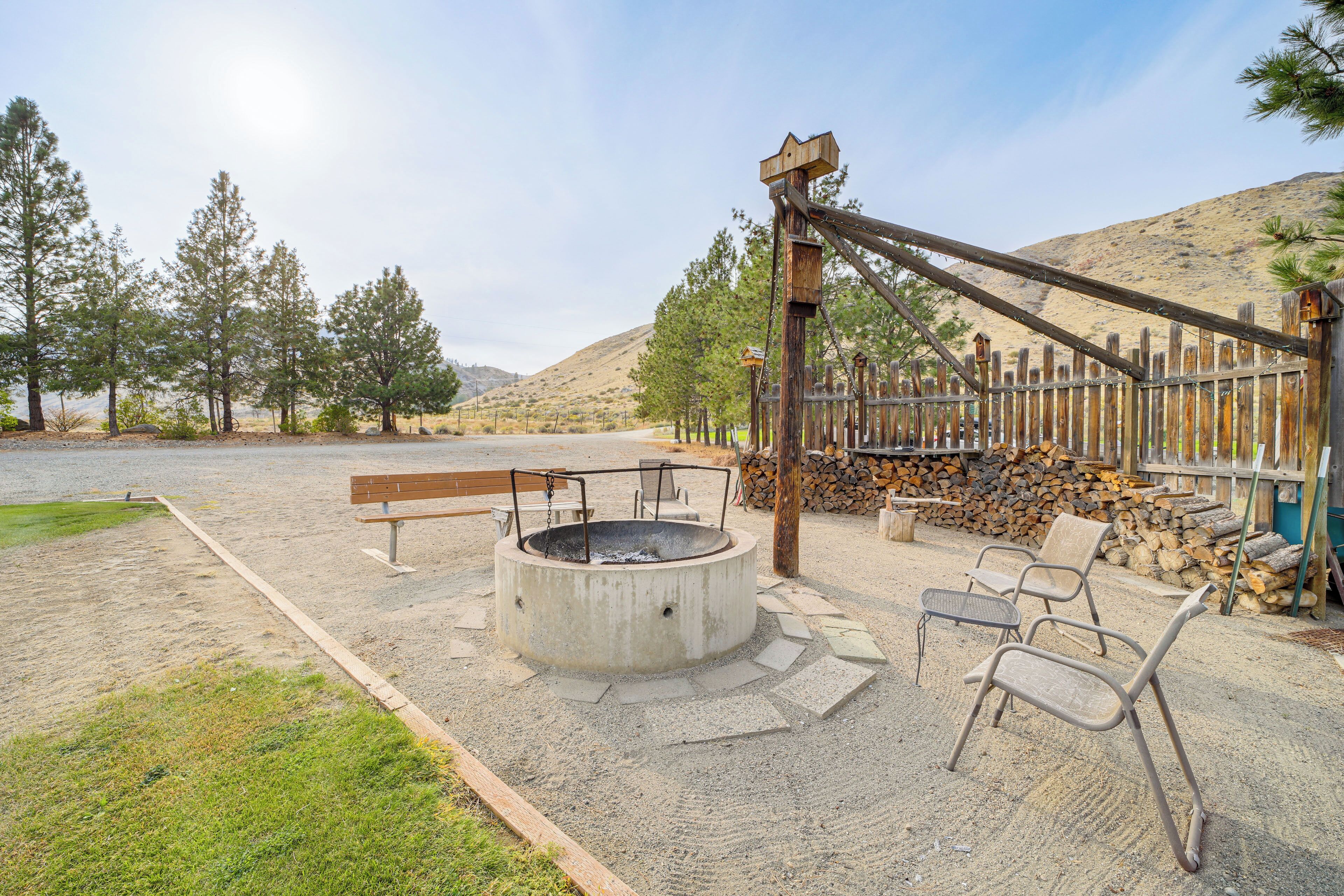 A fire pit area with seating, surrounded by a wooden fence and trees.