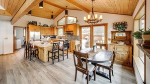 A spacious kitchen with wooden cabinets, a dining area with a large table and chairs, and a high ceiling with exposed beams. - Stunning A-frame Home w/ Views, 10 Mi to Okanogan! (Brewster)