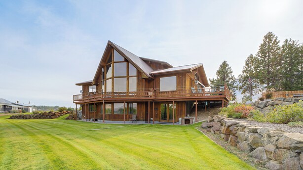 A large, modern two-story house with a prominent balcony, surrounded by a well-maintained lawn and a stone retaining wall. - Stunning A-frame Home w/ Views, 10 Mi to Okanogan! (Brewster)