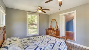 A bedroom with a bed, a dresser, a ceiling fan, and a large window.