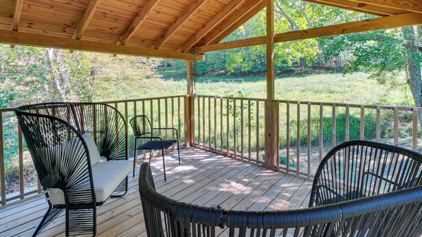 A covered outdoor deck with wooden flooring and metal chairs.