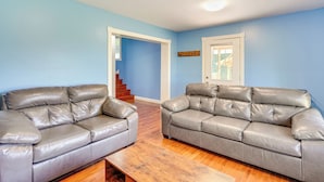 A living room with two grey leather sofas, wooden flooring, a wooden coffee table, and a blue wall.