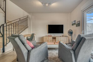 Uma sala de estar moderna com uma televisão de tela plana, sofás cinzentos, uma mesa de centro de madeira e uma escada.