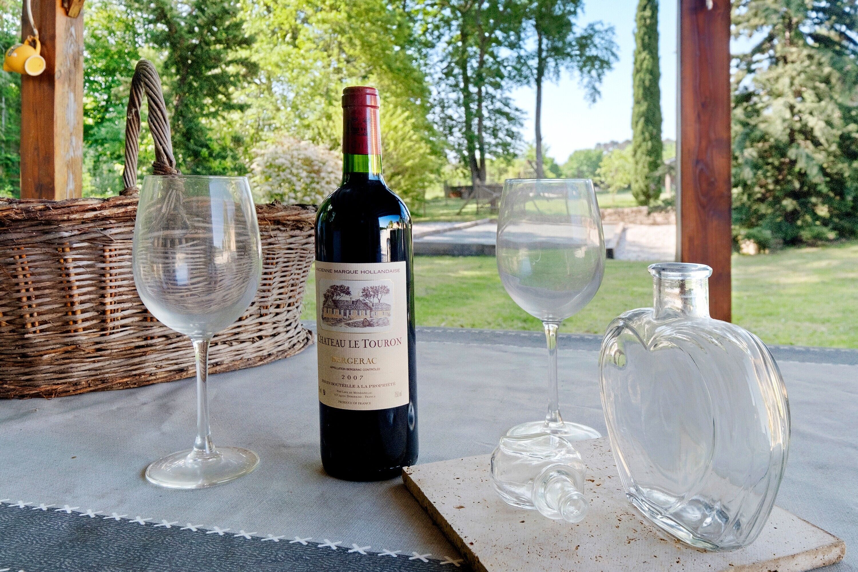 A bottle of Chateau Le Touron wine, two empty wine glasses, and a clear glass decanter on a table.