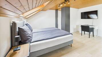 Un dormitorio moderno con techo inclinado, cama, escritorio y televisor.