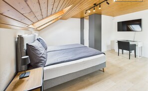 A modern bedroom with a sloped ceiling, a bed, a desk, and a TV.