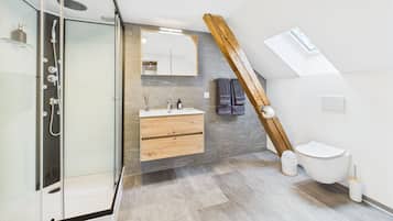 Un baño moderno con cabina de ducha de vidrio, tocador de madera, espejo y retrete.