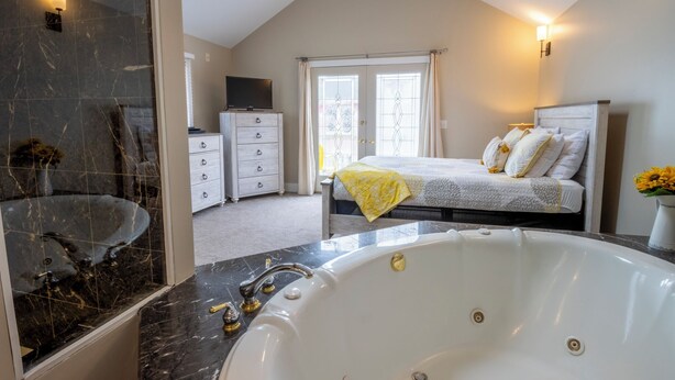 A modern bedroom with a large bed, a bathroom with a bathtub, and a walk-in closet.