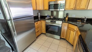 A modern kitchen with stainless steel appliances, wooden cabinets, and a tiled floor.