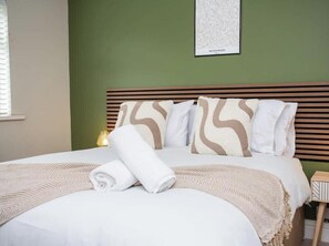 A neatly made bed with a rolled towel, a headboard with a patterned design, and a wall-mounted artwork labeled 'WILLOW BOUQUET.'