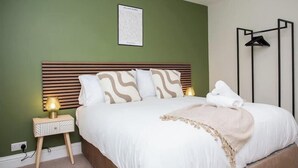 Una cama bien hecha con cabecera, una lámpara de noche y un cuadro enmarcado en la pared.