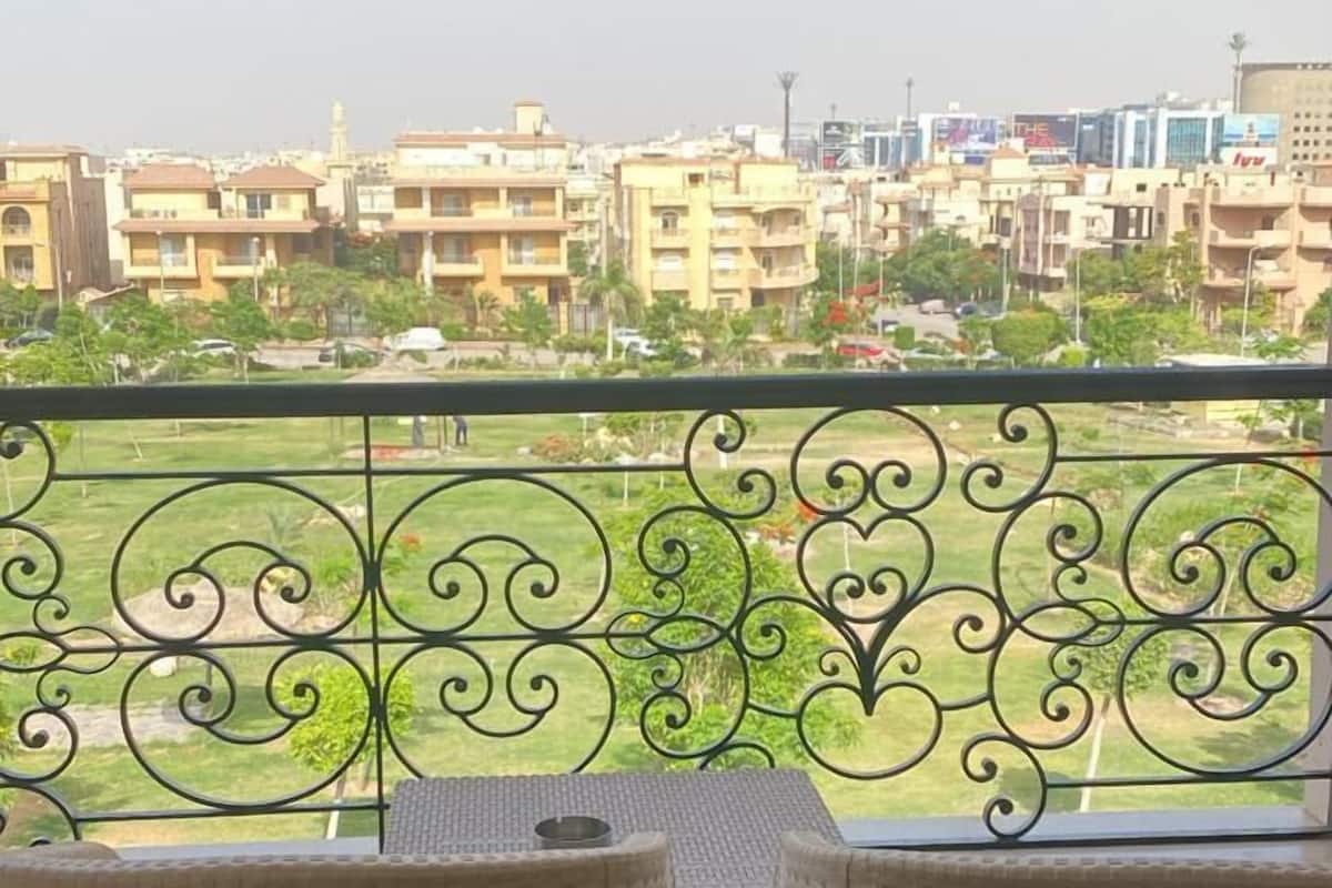 Ein Balkon mit Korbstühlen und Blick auf eine Wohngegend mit Gebäuden und Grünflächen.