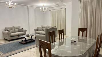 Una sala de estar moderna con una mesa de comedor de vidrio, dos sofás, sillas de madera, una mesa baja y una araña.
