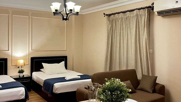 A hotel room with two beds, a dining table with plates and glasses, a chandelier, and an air conditioning unit. - Chelay studios  (New Cairo)