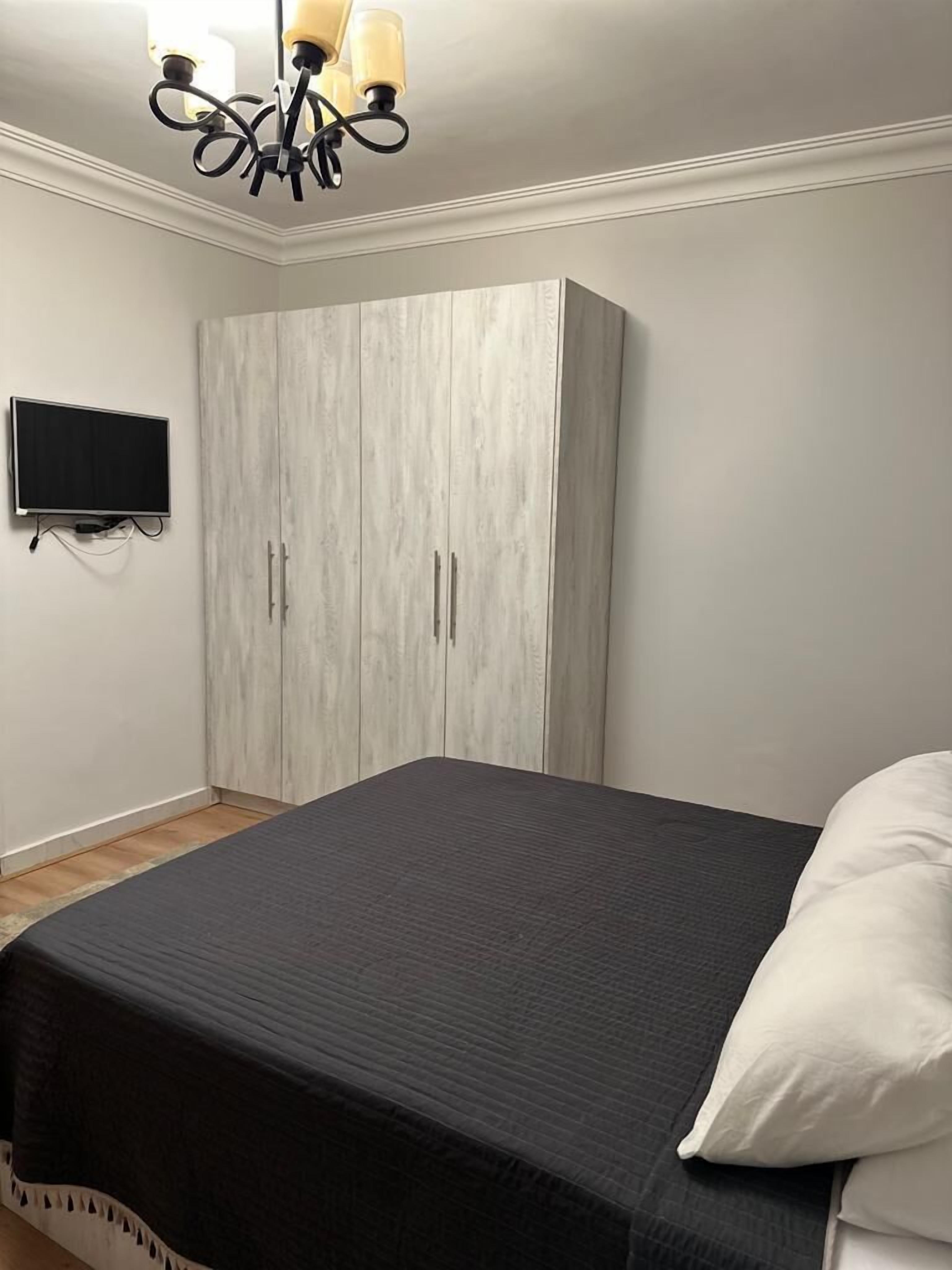 A bedroom with a bed, a wardrobe, a television, and a chandelier.