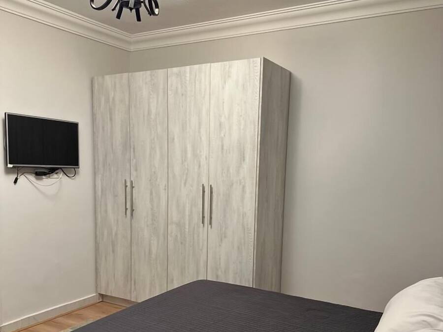 A bedroom with a bed, a wardrobe, a television, and a chandelier.