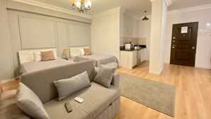 A modern hotel room with a sofa, two beds, a kitchenette, and a wooden floor. - Chelay studios  (New Cairo)