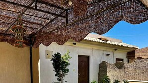 An outdoor patio with wicker furniture, a potted plant, and a small building with a door. - Chelay studios  (New Cairo)