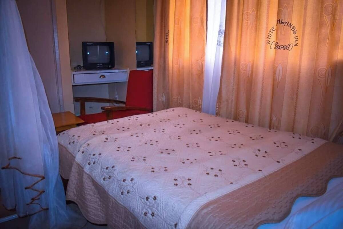 Un dormitorio con una cama, dos mesitas de noche, un escritorio y dos televisores.