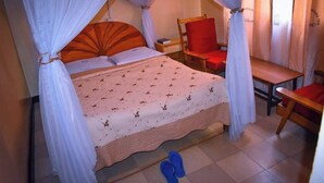 A bedroom with a bed, a chair, a nightstand, and a pair of slippers on the floor. - White highlands Inn Eldoret (Eldoret)