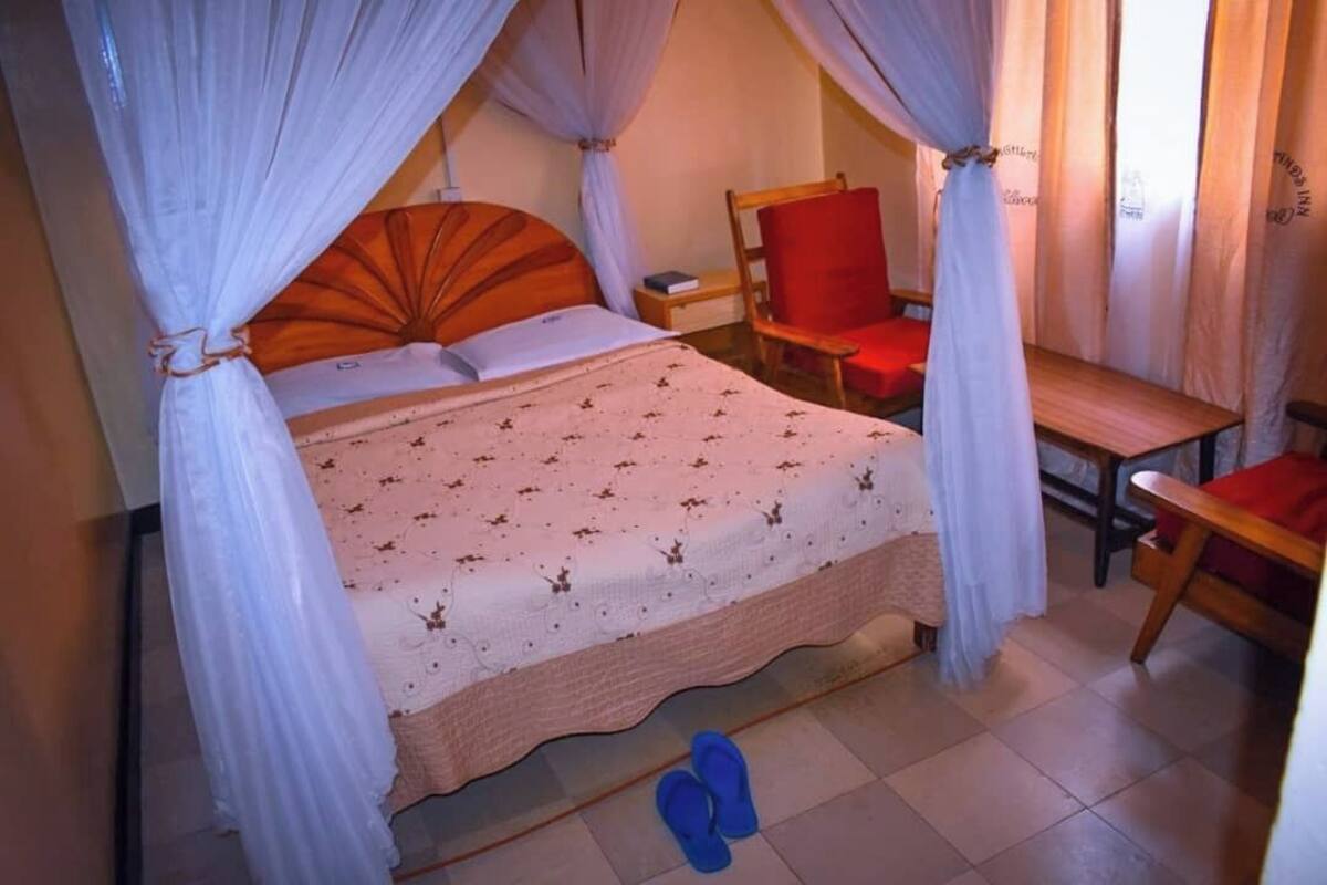 Un dormitorio con una cama, una silla, una mesita de noche y un par de pantuflas en el suelo.