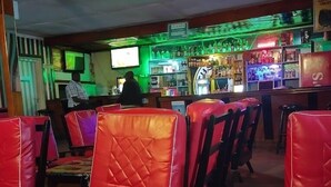 A restaurant interior with red leather chairs, a bar area with various bottles, and a television screen. - White highlands Inn Eldoret (Eldoret)