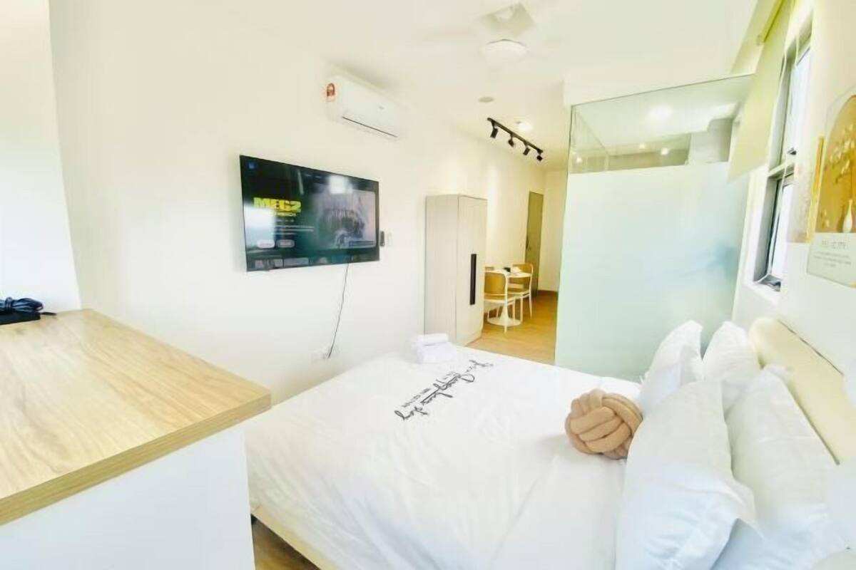 A hotel room with a bed, a TV mounted on the wall, a wooden desk, and a chair.
