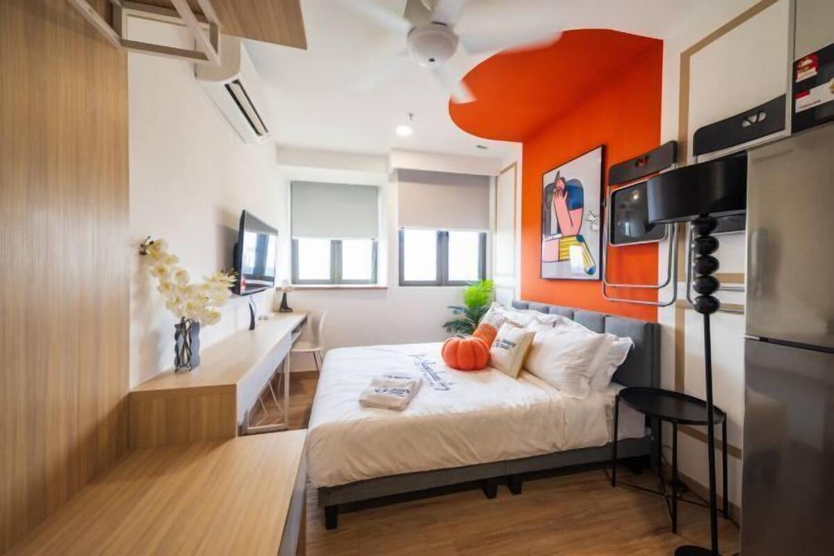 A modern bedroom with a bed, a desk, a chair, a TV, and a refrigerator.