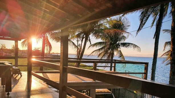 Ein überdachter Außenbereich mit Blick auf das Meer und Palmen.