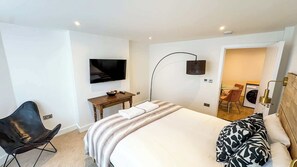 A hotel room with a bed, a TV mounted on the wall, a desk with a chair, a washing machine, and a mirror.