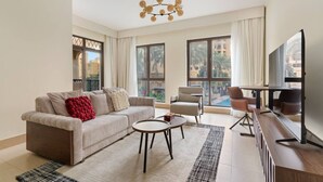 Un salon moderne comprenant un canapé, des fauteuils, une table basse et un téléviseur. De grandes fenêtres offrent une vue sur l’extérieur.