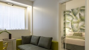 Et moderne soveværelse med en grøn sofa, en seng med en palmebladstapet bagvæg og et lille skrivebord med en stol.