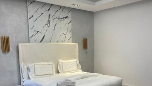Ein modernes Schlafzimmer mit einem großen Bett, einem Nachttisch, einer Marmorwand und einer Deckenleuchte.