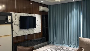 Ein modernes Wohnzimmer mit einem großen Fernseher an einer Marmorwand, einer Kristallleuchtre und einem Sofa mit gemusterten Kissen.