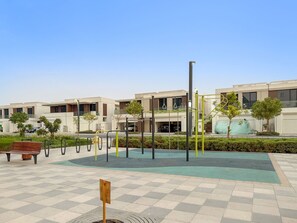 A modern outdoor area with a checkered floor, a wooden bench, exercise equipment, and a covered seating area. - Luxury Unit: Balcony Views, Full Kitchen, 15 Min Burj Khalifa (MBR)