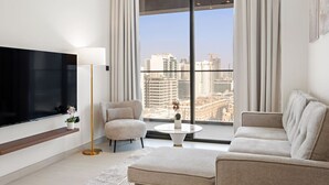 Ein modernes Wohnzimmer mit großem Fernseher, einer Couch, einem Sessel, einem kleinen Tisch mit Pflanze und Blick auf die Stadt durch große Fenster.