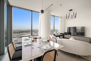 Un espace repas moderne avec une grande table dressée pour six personnes, un canapé, un téléviseur et une vue sur la ville.