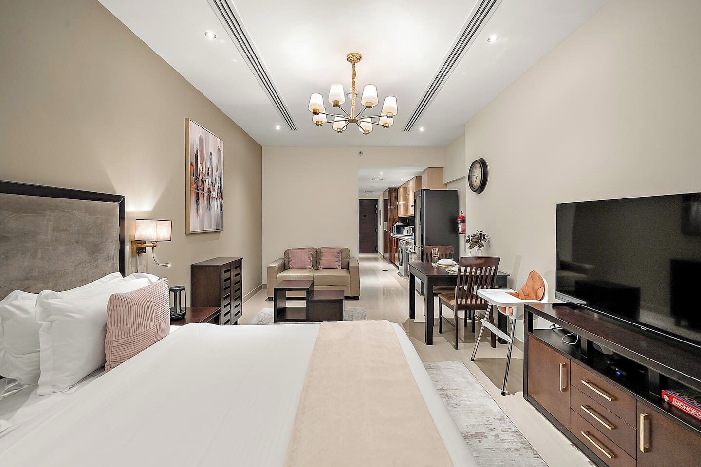A hotel room with a large bed, a television, a dining area, and a kitchen.